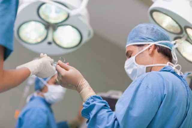 medico recebendo uma tesoura para fazer cirurgia