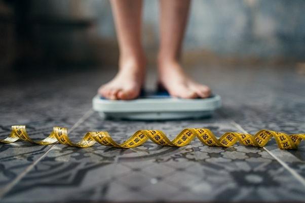 pés de pessoa com obesidade em cima de uma balança com uma fita métrica na frente