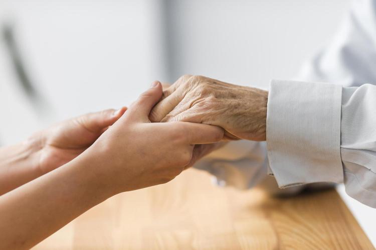 Profissional de saúde segurando as mãos de idosa com tremor