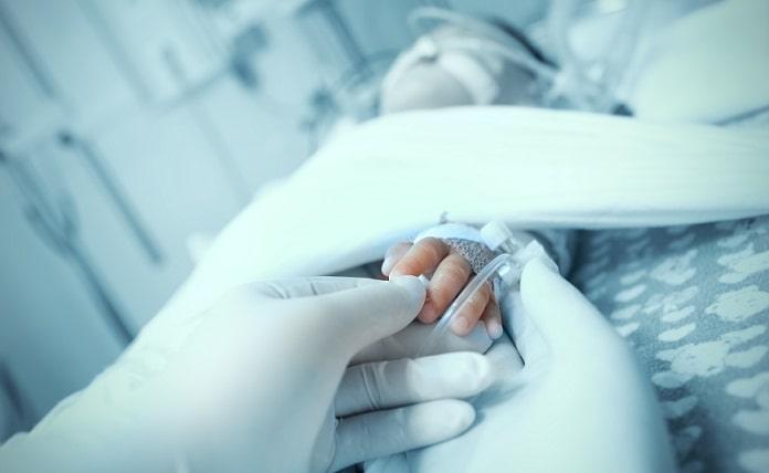 bebê com apneia da prematuridade em UTI pediátrica, mãos do médico segurando a mão do bebê em foco