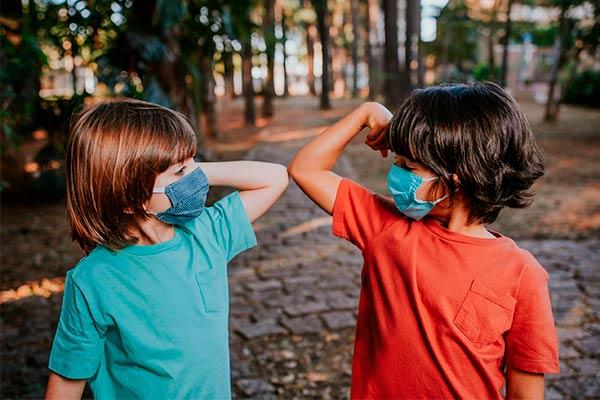 duas crianças com máscara de proteção fazendo contato pelos cotovelos