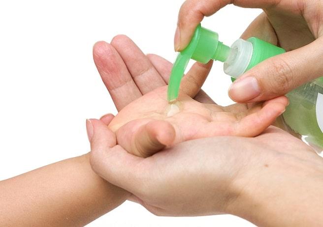 mão de adulto colocando alcool em gel em mão de criança, para prevenir acidentes domésticos
