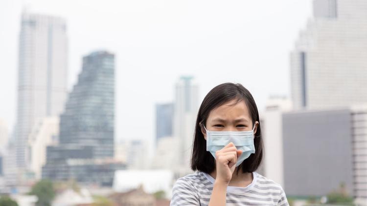 Menina oriental de máscara em meio à poluição representando os danos das alterações climáticas à saúde infantil