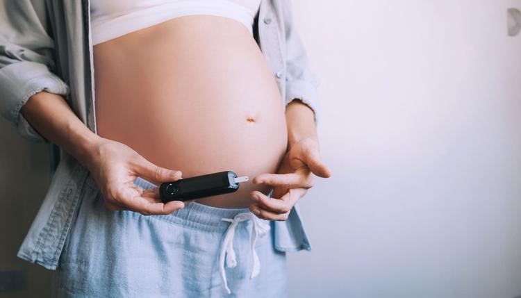 Grávida segurando medidor de glicose ao lado da barriga representando a diabetes na gestação