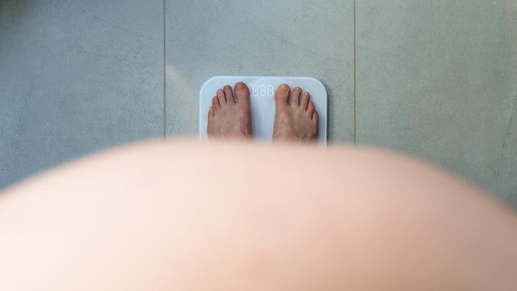 Pessoa obesa se pesando na balança como estratégia para manutenção do peso perdido